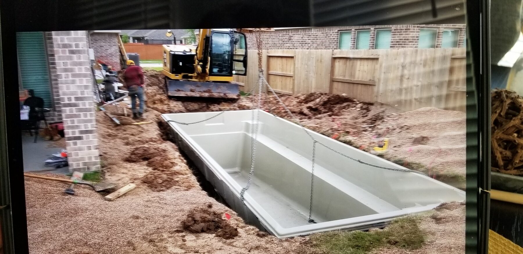 Fiberglass pool installation in progress with excavator
